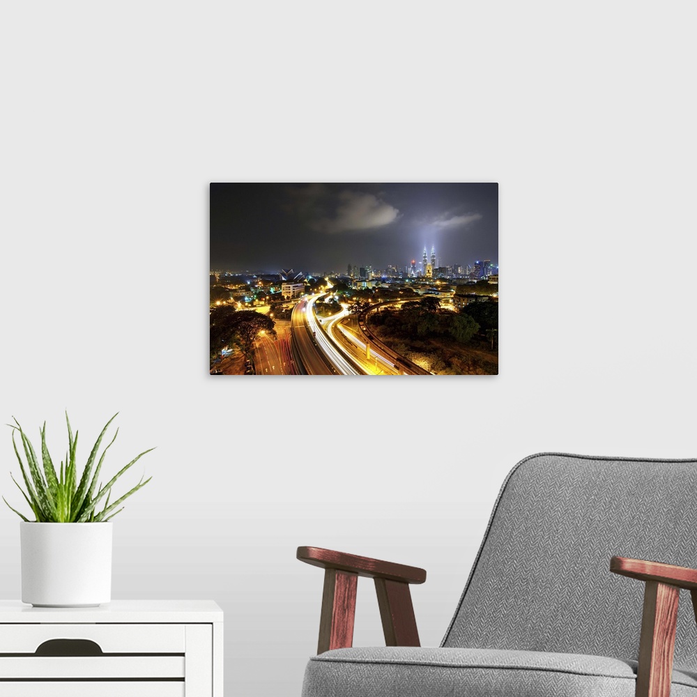 A modern room featuring Kuala Lumpur skyline and long exposure road at dusk.