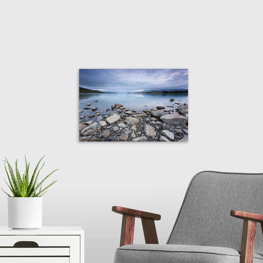 A modern room featuring Lake Tekapo in New Zealand, with rocks in foreground during morning cloud.