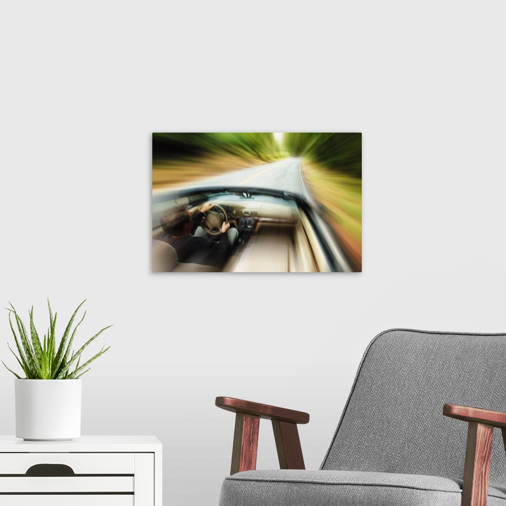A modern room featuring lifestyle photograph of a caucasian man driving fast down a road in a convertible