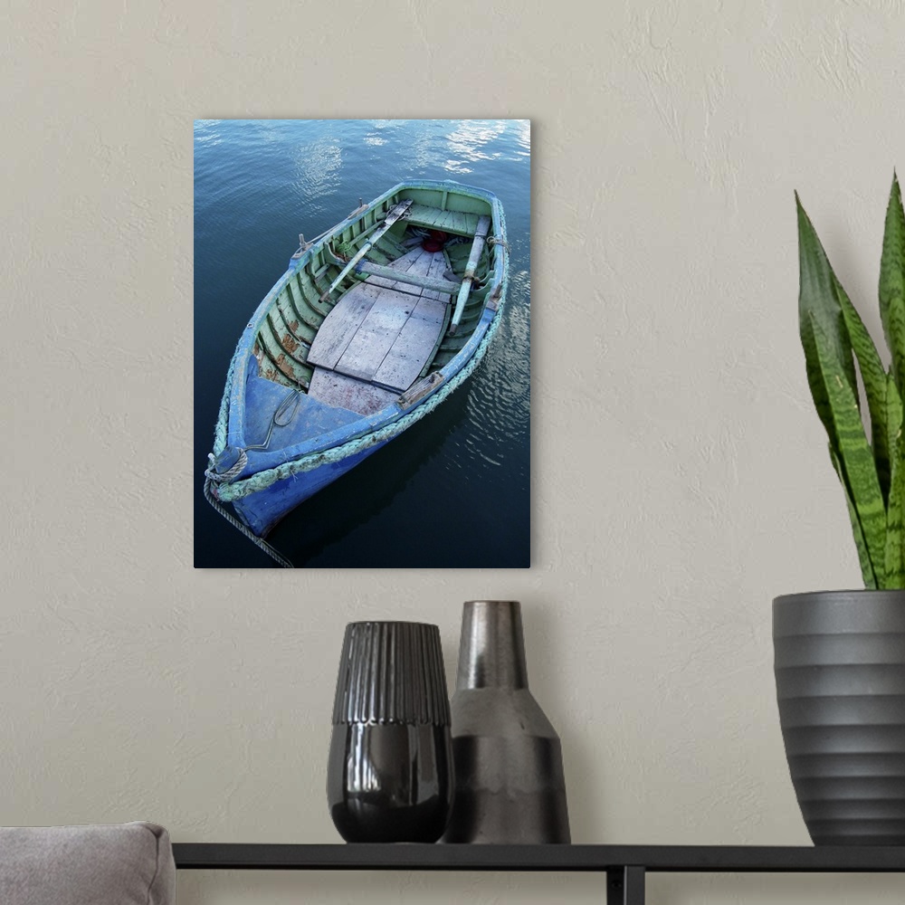 A modern room featuring Rustic wooden fishing boat moored in calm waters in fishing village of Marsaxlokk, Malta.