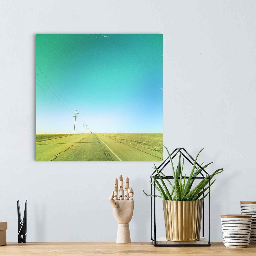 A bohemian room featuring Lone car on simple country road with clear blue sky and telephone lines.