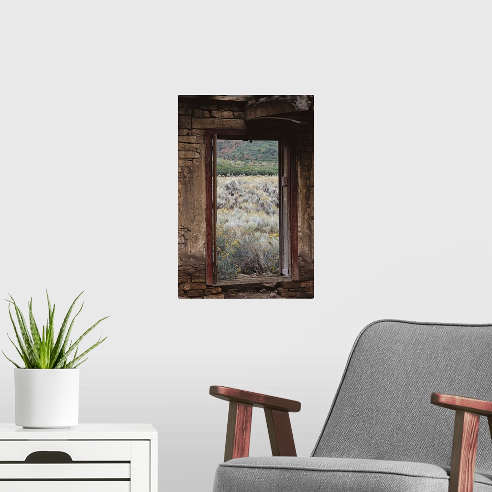 A modern room featuring looking out of an abandoned adobe cabin to see sage brush and dead grass