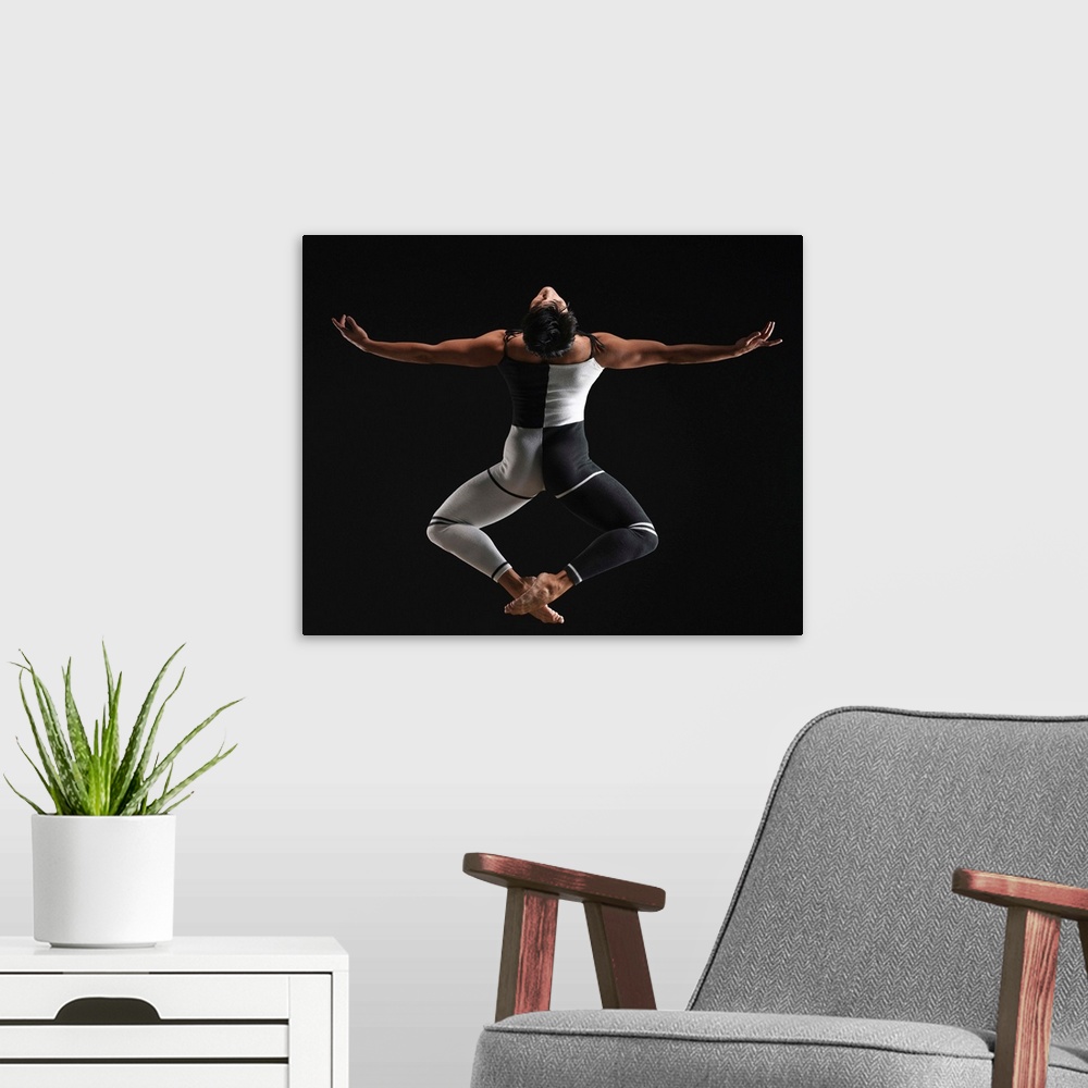 A modern room featuring Male ballet dancer in mid air pose, arms extended, rear view