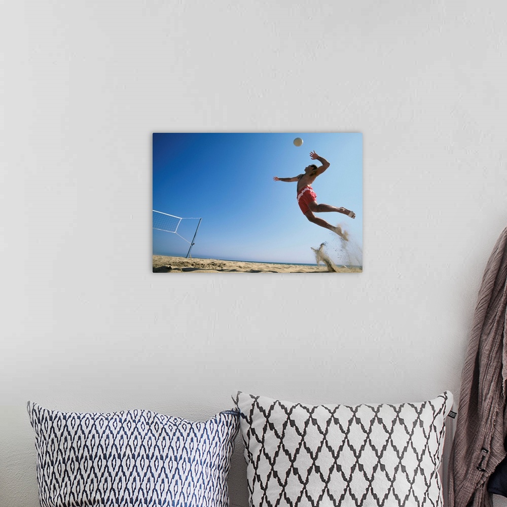 A bohemian room featuring Male beach volleyball player jumping up to spike ball. California, USA.