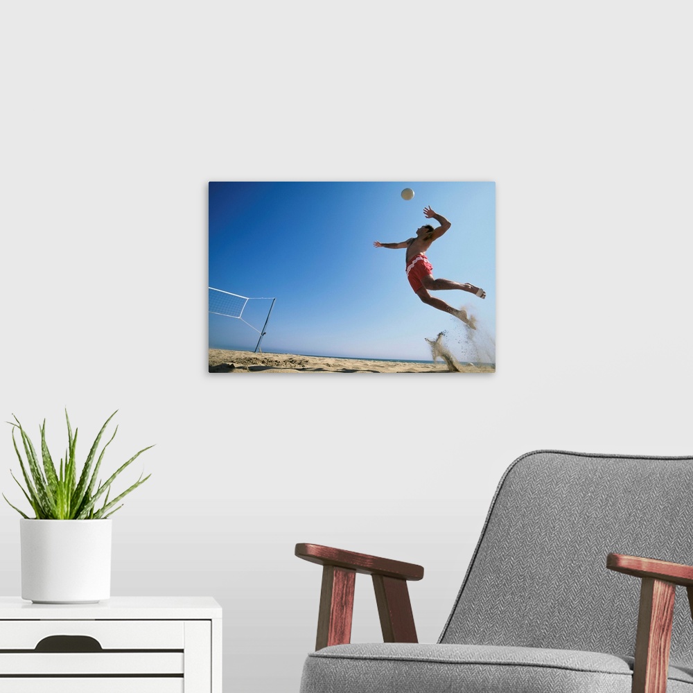 A modern room featuring Male beach volleyball player jumping up to spike ball. California, USA.