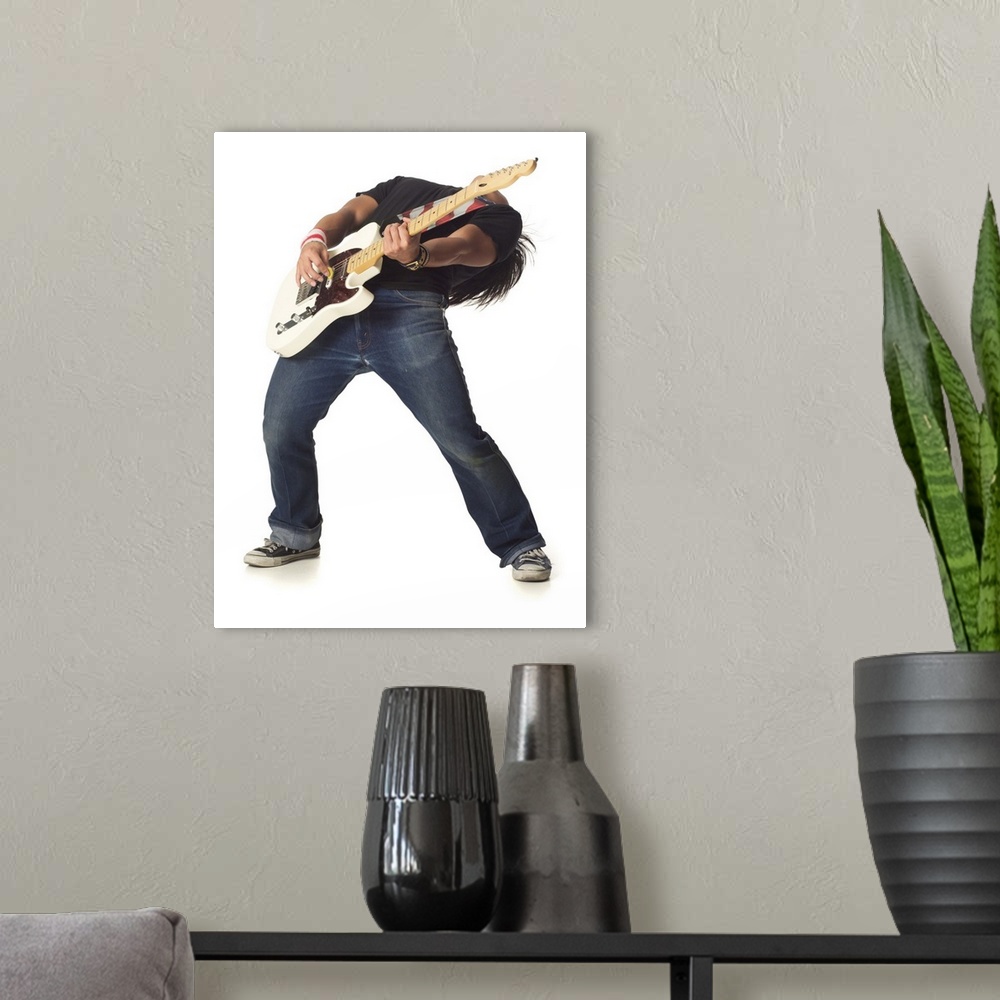 A modern room featuring an asian male teen in jeans and a black shirt leans back while playing an electric guitar