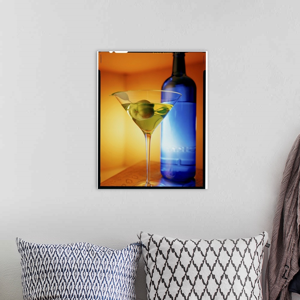 A bohemian room featuring Big vertical photograph of fruit martini in a glass, sitting on a counter in front of a blue bottle.