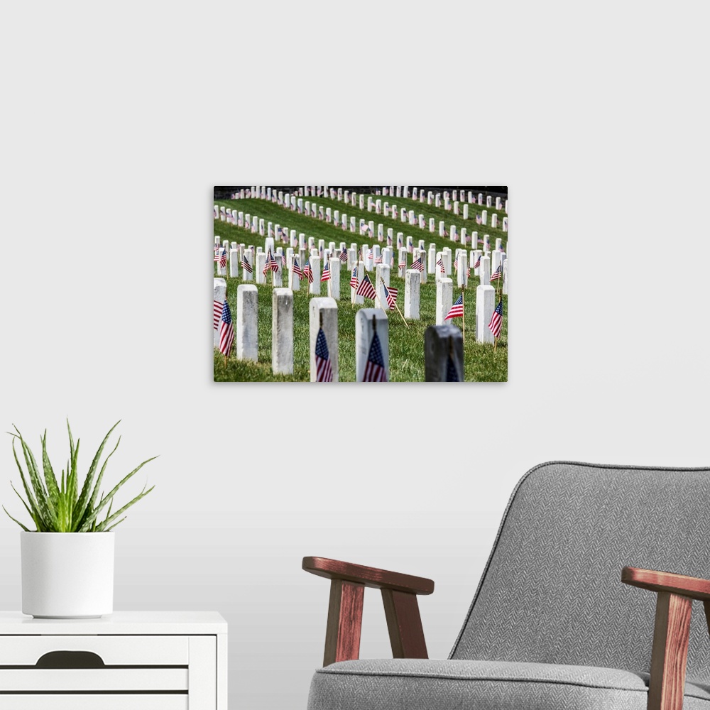A modern room featuring America flags stand in front of rows of white uniform gravestones at the well maintained grassy A...