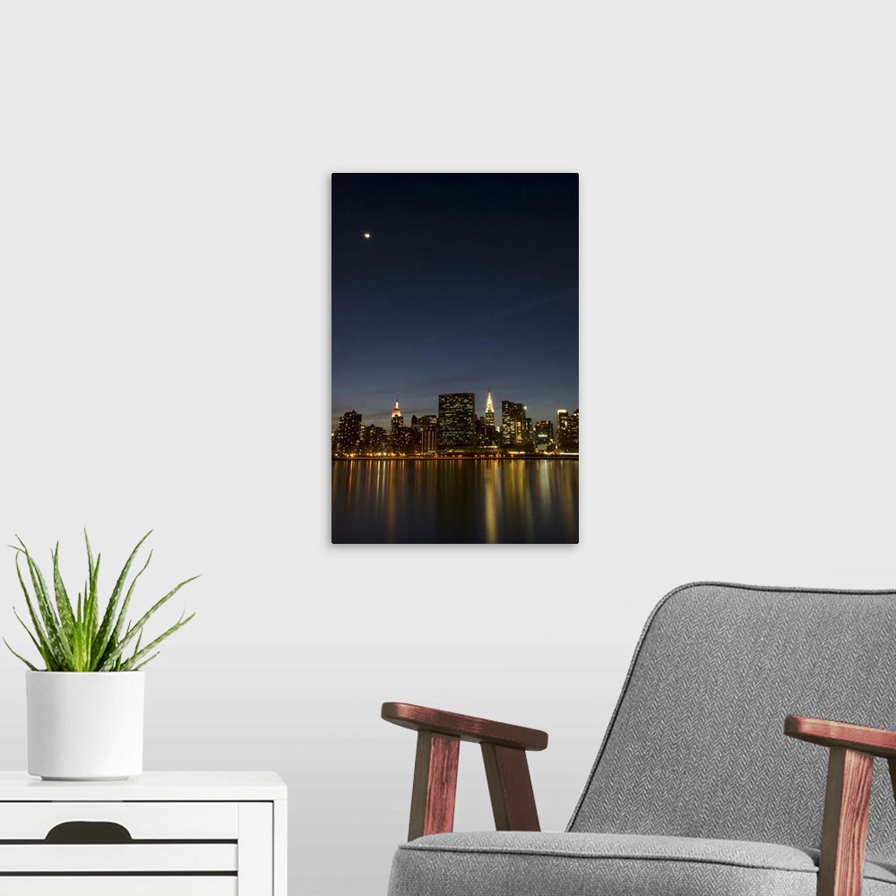 A modern room featuring Midtown Manhattan at dusk with the moon above and reflection of the building lights in the East R...