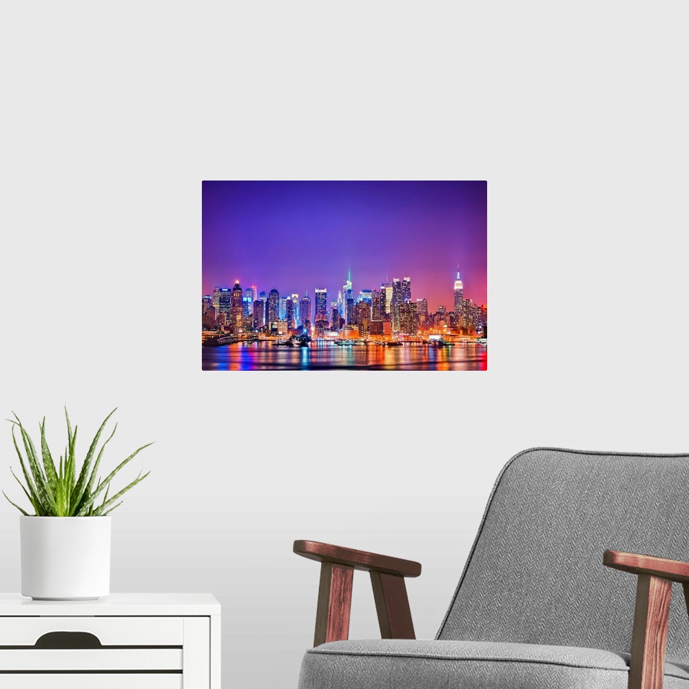 A modern room featuring Photograph of New York skyline at night with the Hudson River in foreground.  The building lights...