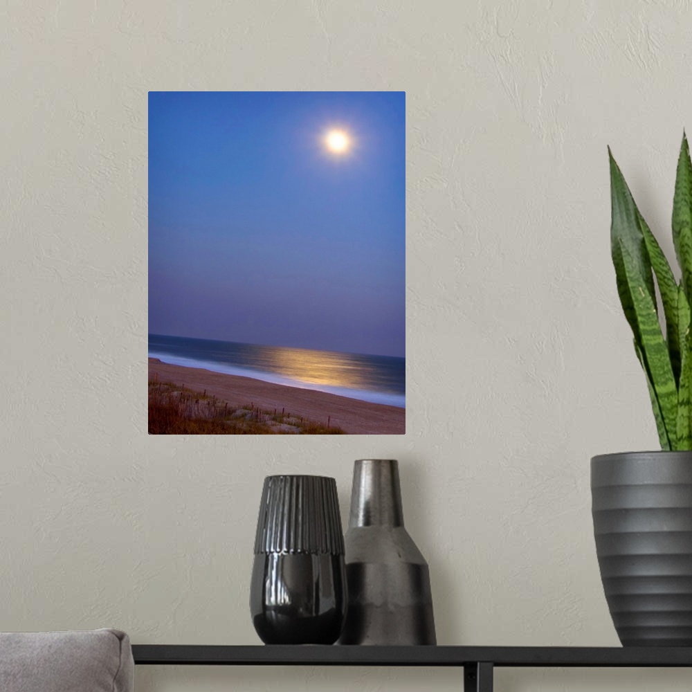 A modern room featuring This large piece is a picture of the moon shining brightly over the beach and reflecting in the o...