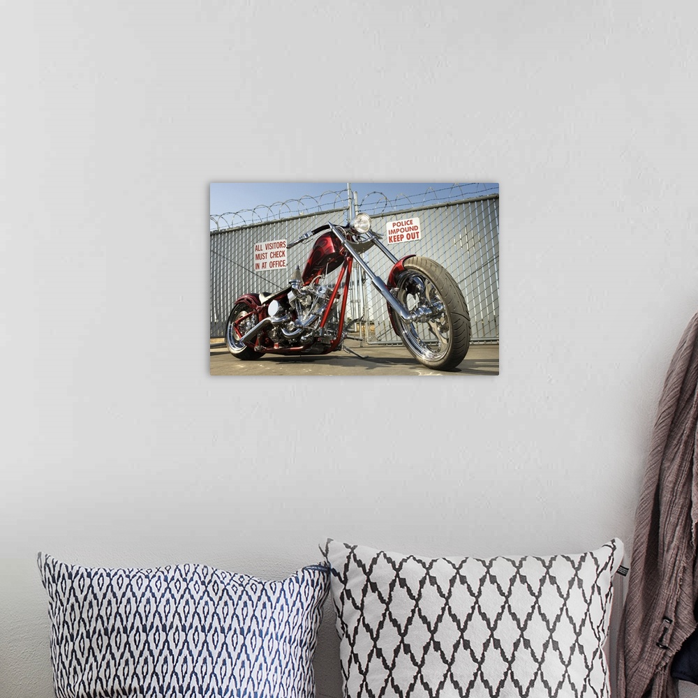A bohemian room featuring A chrome and red motorcycle sits on the the conrete pavement infront of a barbed wire fence surro...