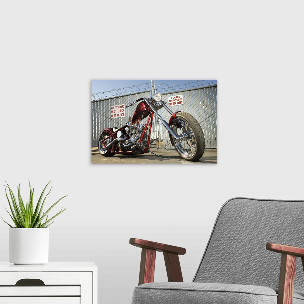 A modern room featuring A chrome and red motorcycle sits on the the conrete pavement infront of a barbed wire fence surro...