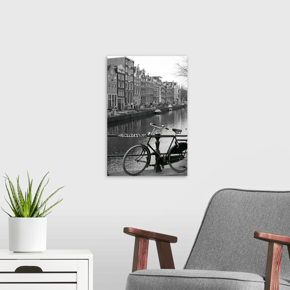 A modern room featuring Vertical canvas photo art of a bike leaning against a railing in front of a river running through...