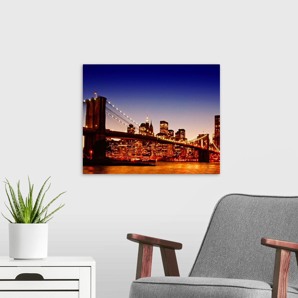 A modern room featuring Large photograph of the Brooklyn bridge with a sun kissed river below at dusk with NYC lit up in ...