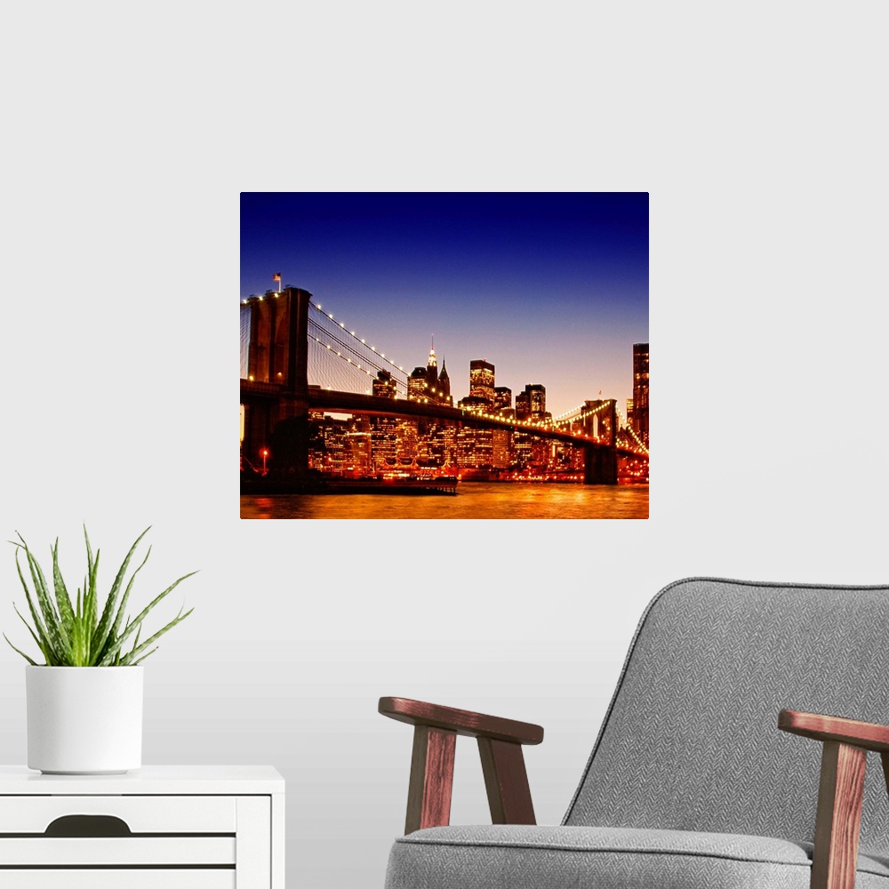A modern room featuring Large photograph of the Brooklyn bridge with a sun kissed river below at dusk with NYC lit up in ...
