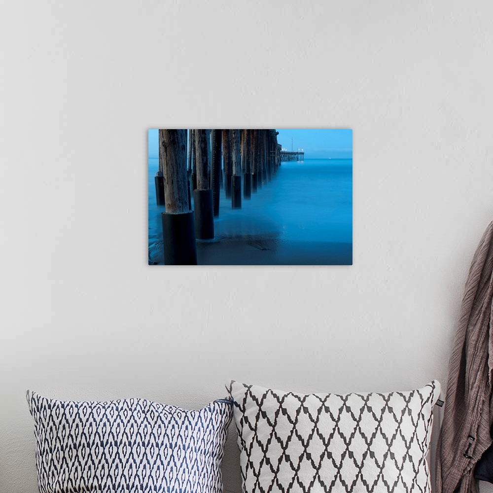 A bohemian room featuring Large print of tall wooden pier pillars holding up a pier leading into the ocean from the shore.
