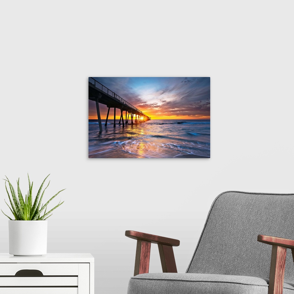 A modern room featuring Sun intersects pier at sunset with colorful waves and sky.
