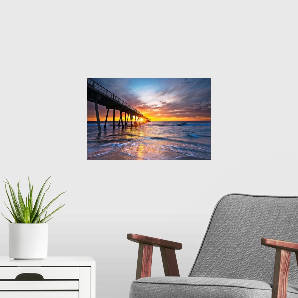 A modern room featuring Sun intersects pier at sunset with colorful waves and sky.