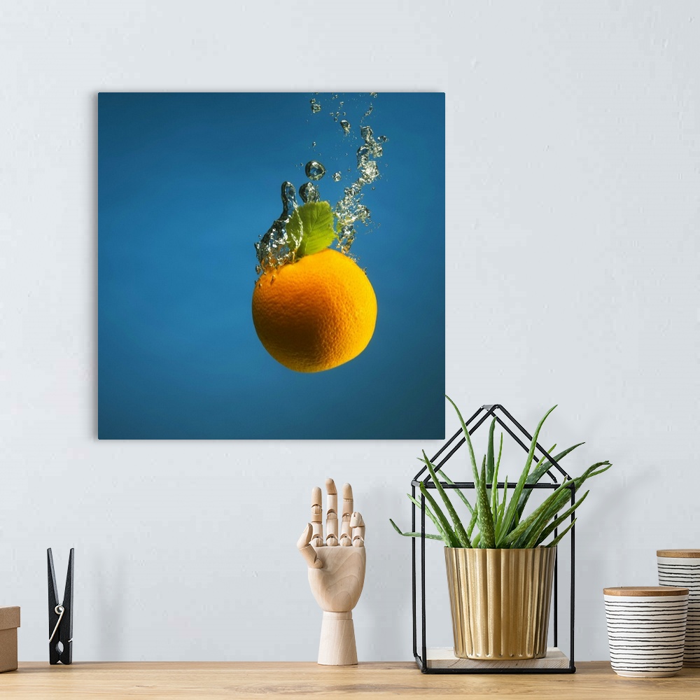 A bohemian room featuring an orange splashed into water, creating bubbles, shot on blue backdrop