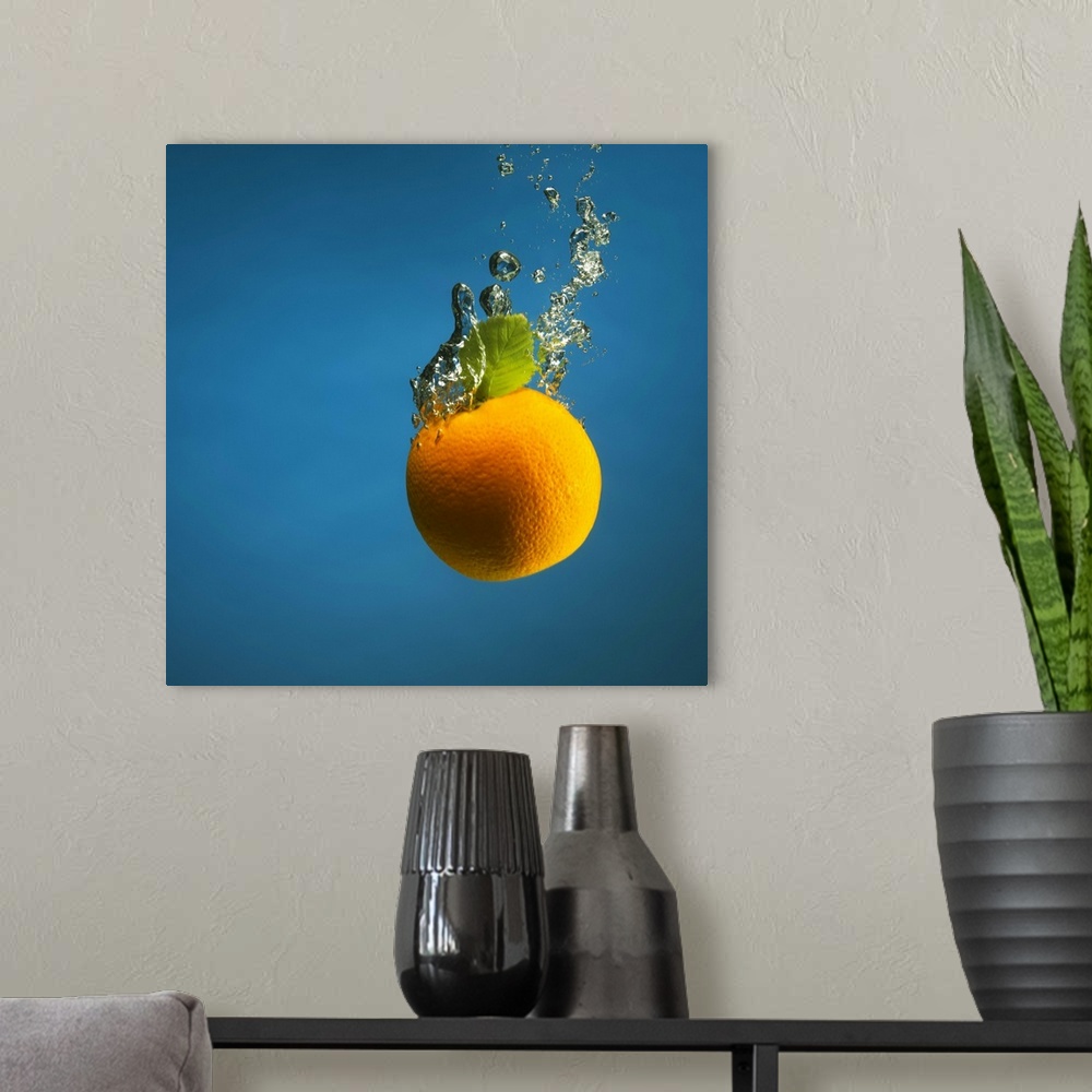 A modern room featuring an orange splashed into water, creating bubbles, shot on blue backdrop