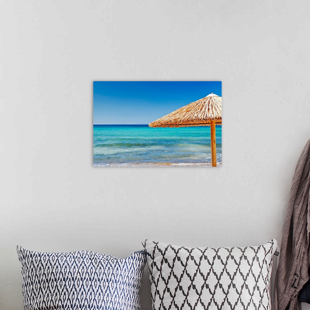 A bohemian room featuring Photograph of straw umbrella near shoreline under a clear bright sky.