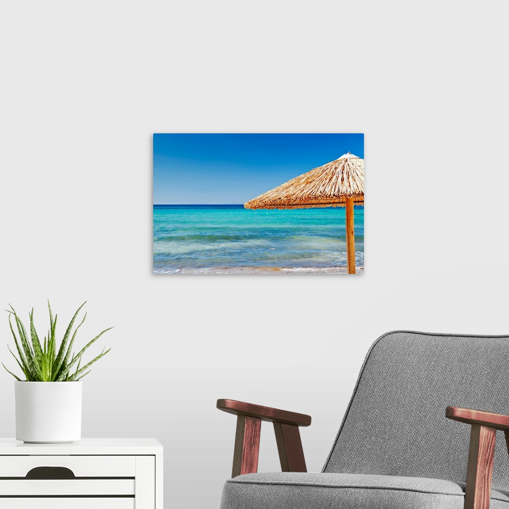 A modern room featuring Photograph of straw umbrella near shoreline under a clear bright sky.
