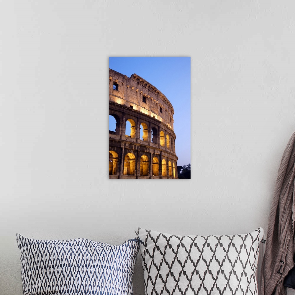 A bohemian room featuring Veridical photograph of the Roman Coliseum at dusk with the lights illuminating the arched windows.