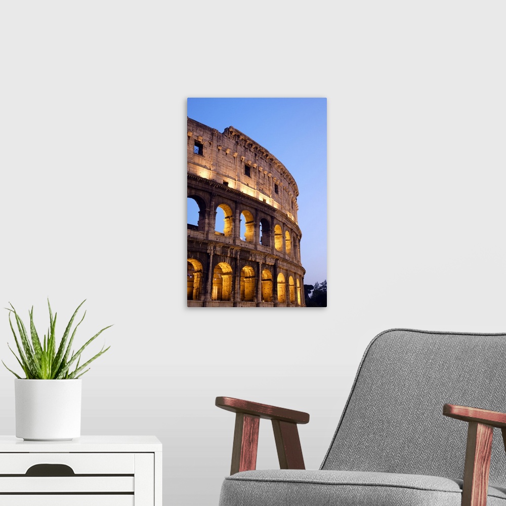 A modern room featuring Veridical photograph of the Roman Coliseum at dusk with the lights illuminating the arched windows.