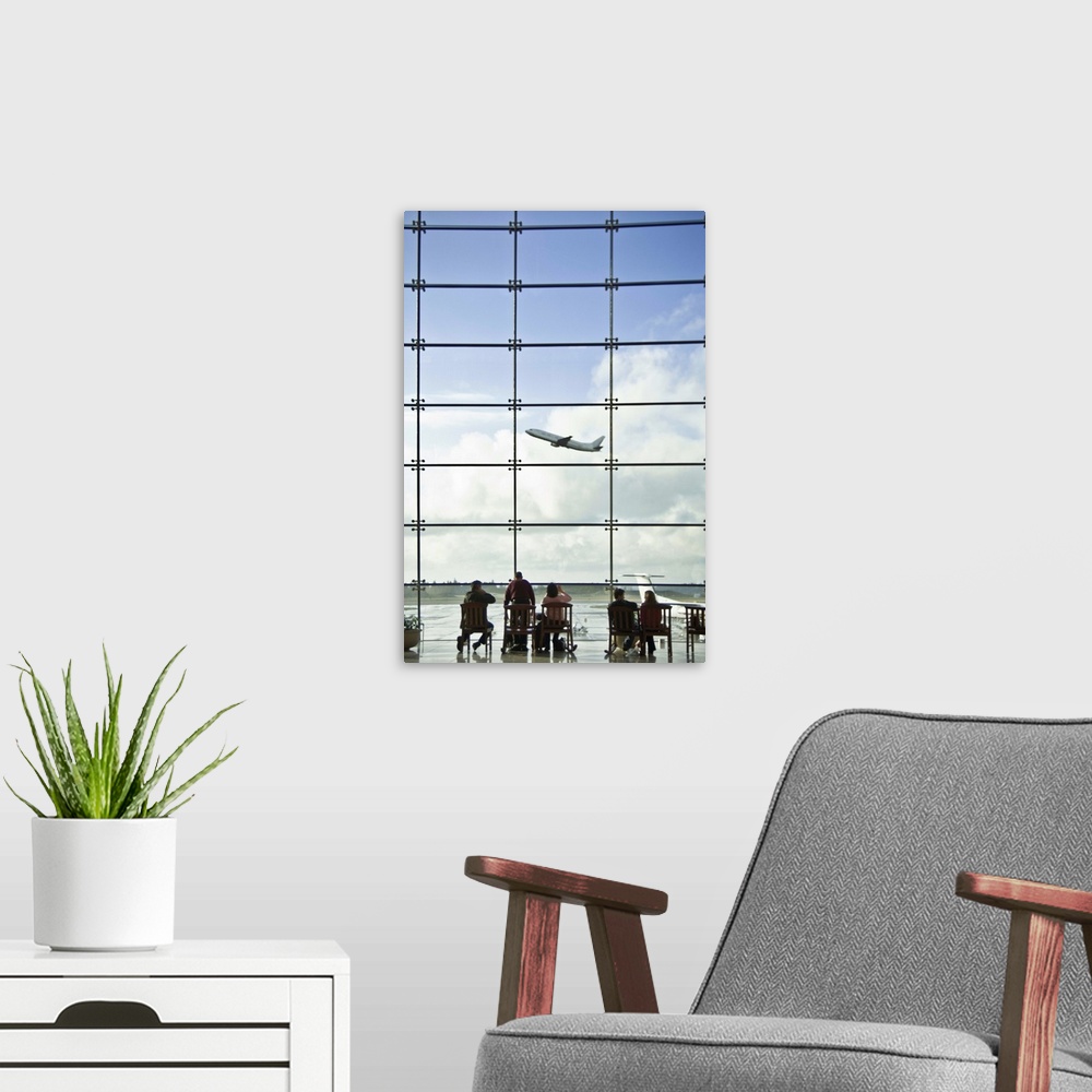 A modern room featuring People sitting in airport lobby and looking at airplane taking off