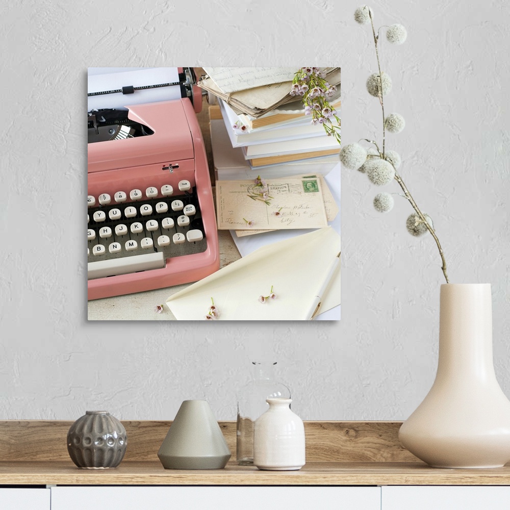 A farmhouse room featuring A pink typewriter surrounded by old books, letters and dried flowers in this square shaped, decor...