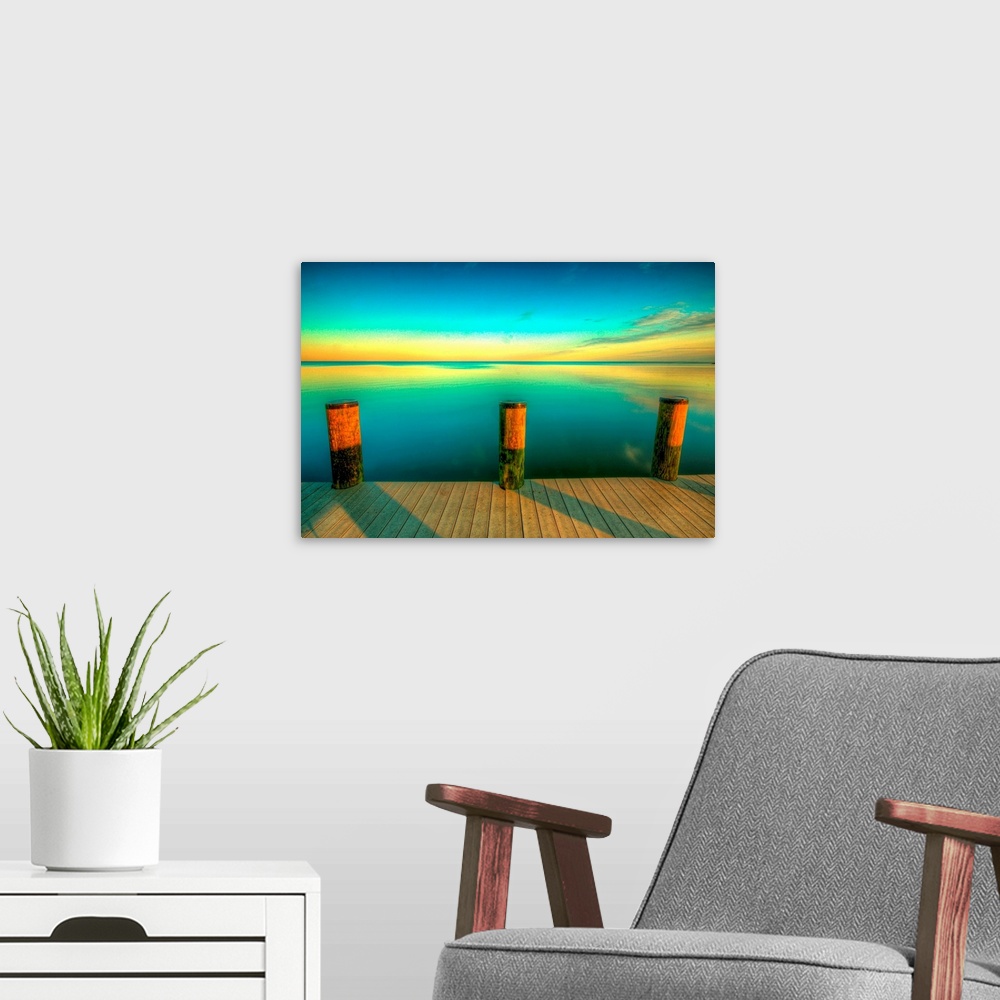 A modern room featuring Big canvas photo art of a dock looking off onto calm water at sunset with the sky colors reflecti...