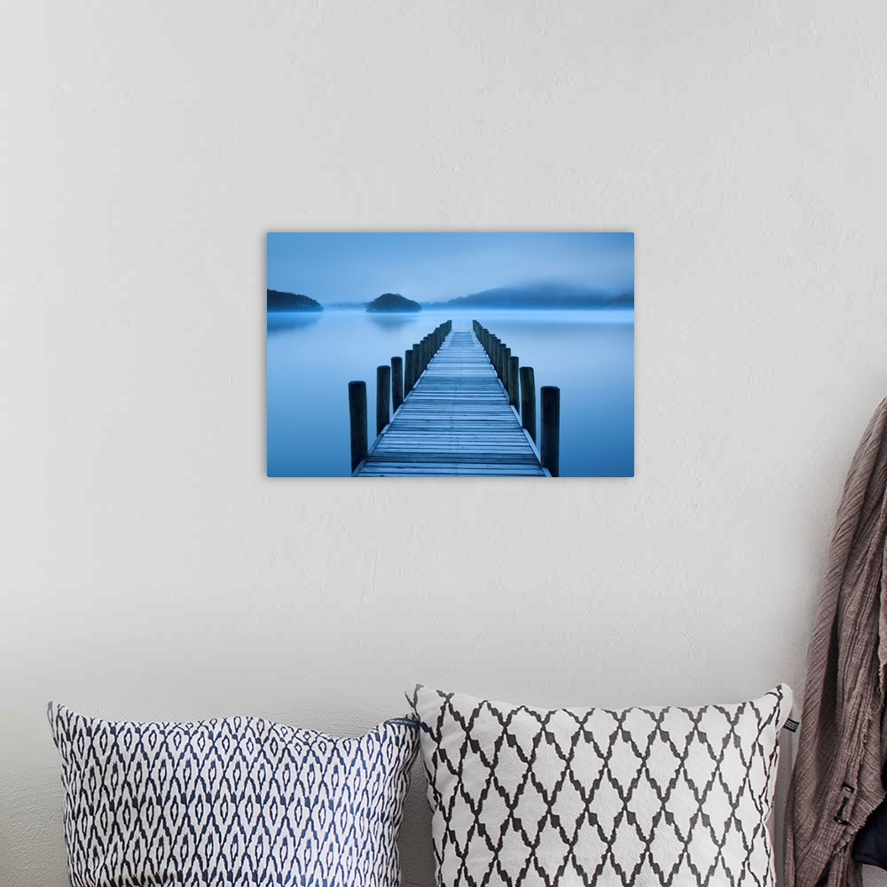 A bohemian room featuring A photograph is taken looking down a pier that stands over a body of water and looks out onto roc...