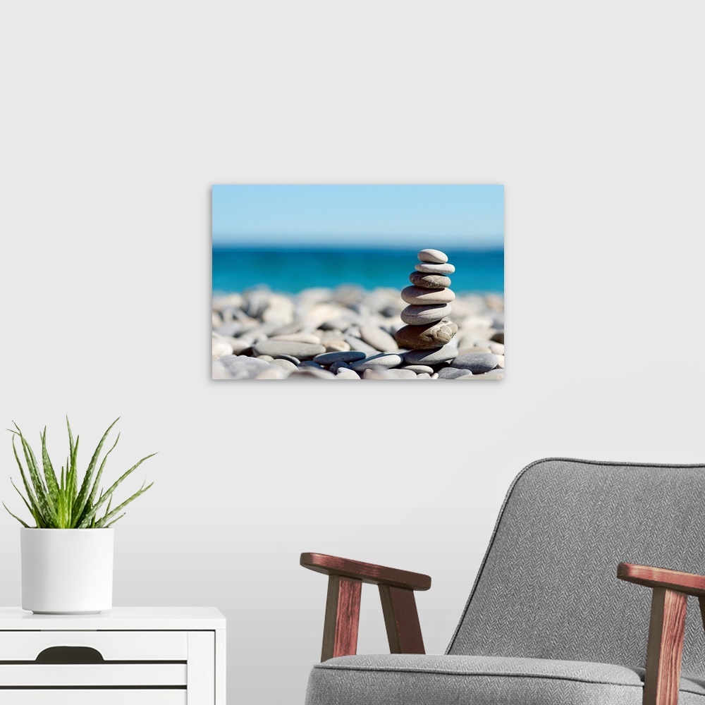 A modern room featuring Up-close photograph of seven smoothed pebbles stacked on top of each other sitting on top of a be...