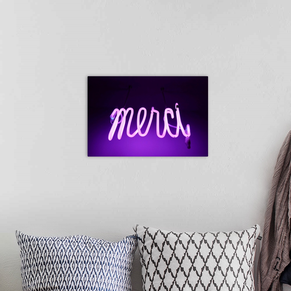 A bohemian room featuring Pink and purple Neon light sign saying merci (thanks in french).