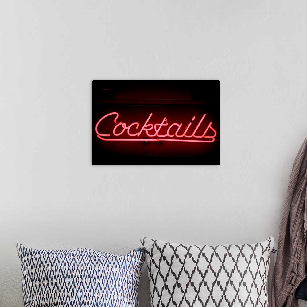 A bohemian room featuring An illuminated pink sign with the work cocktails sits on a dark wall.