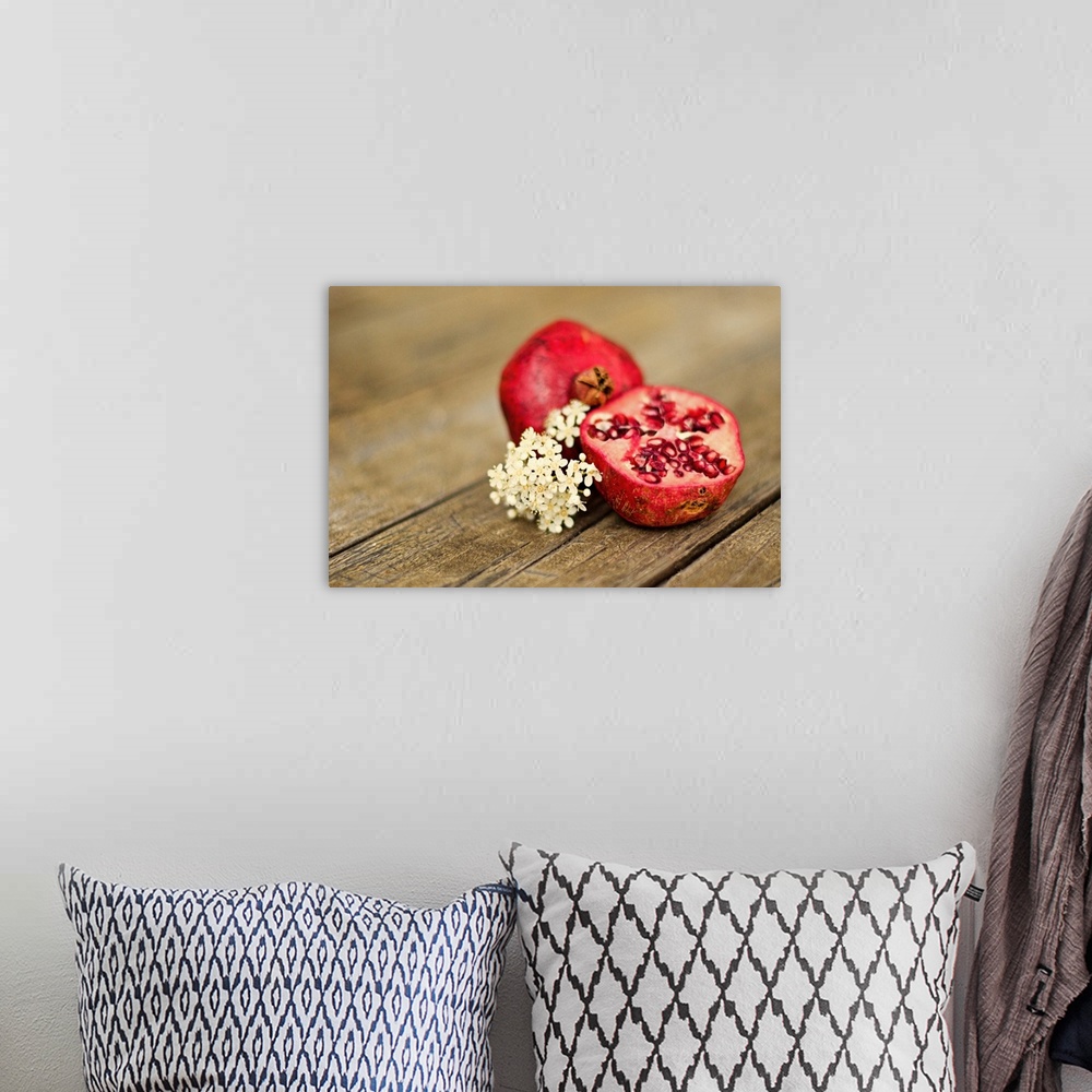 A bohemian room featuring Pomegranate fruit cut in half, with cluster of tiny white flowers on rustic looking wooden tabletop.
