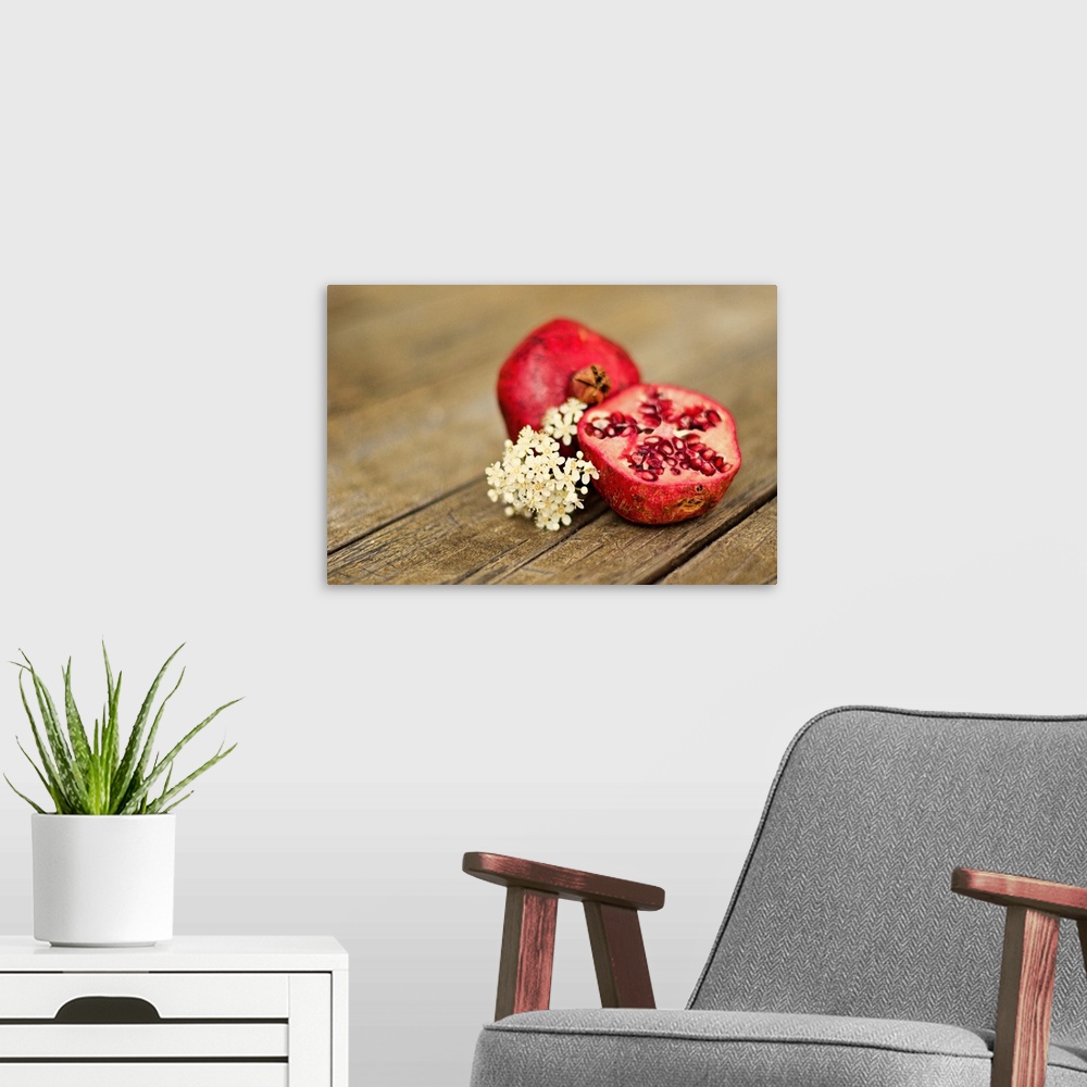 A modern room featuring Pomegranate fruit cut in half, with cluster of tiny white flowers on rustic looking wooden tabletop.