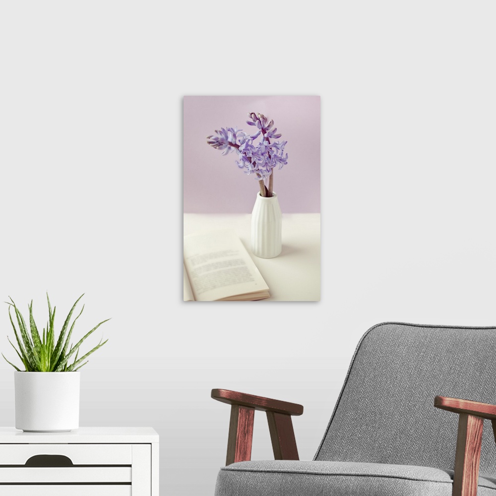 A modern room featuring Purple flower vase with open book on table.