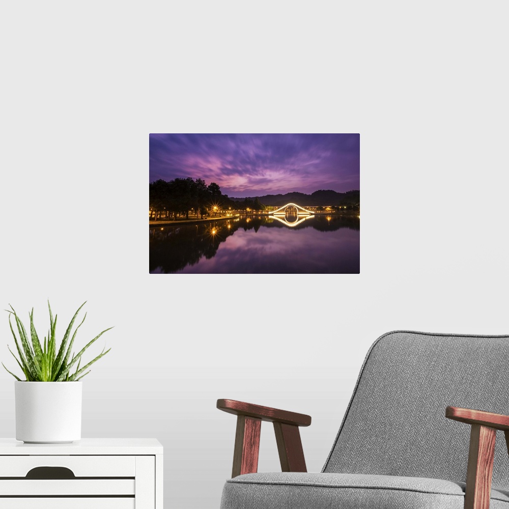 A modern room featuring Purple tone prior to sunrise with light up arch bridge and its reflection in the water.