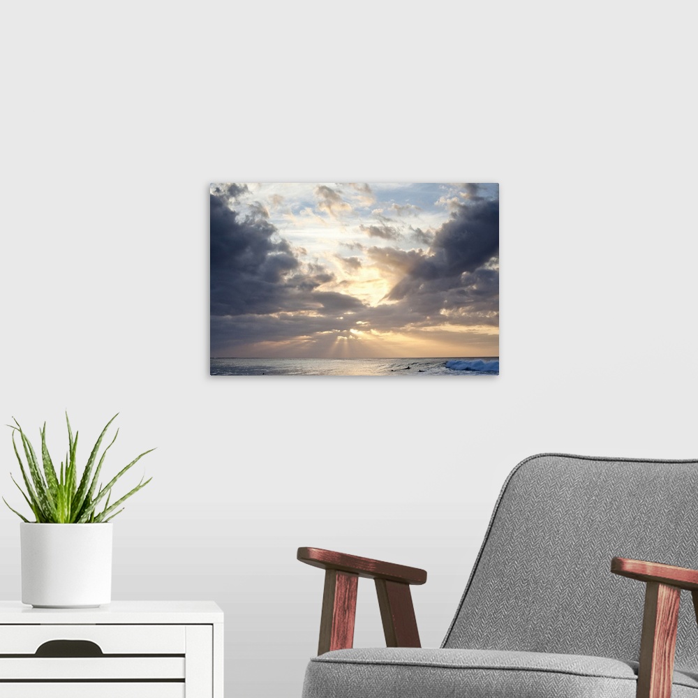 A modern room featuring Crepuscular rays of light break through the sky over the blue ocean, surfers in the background