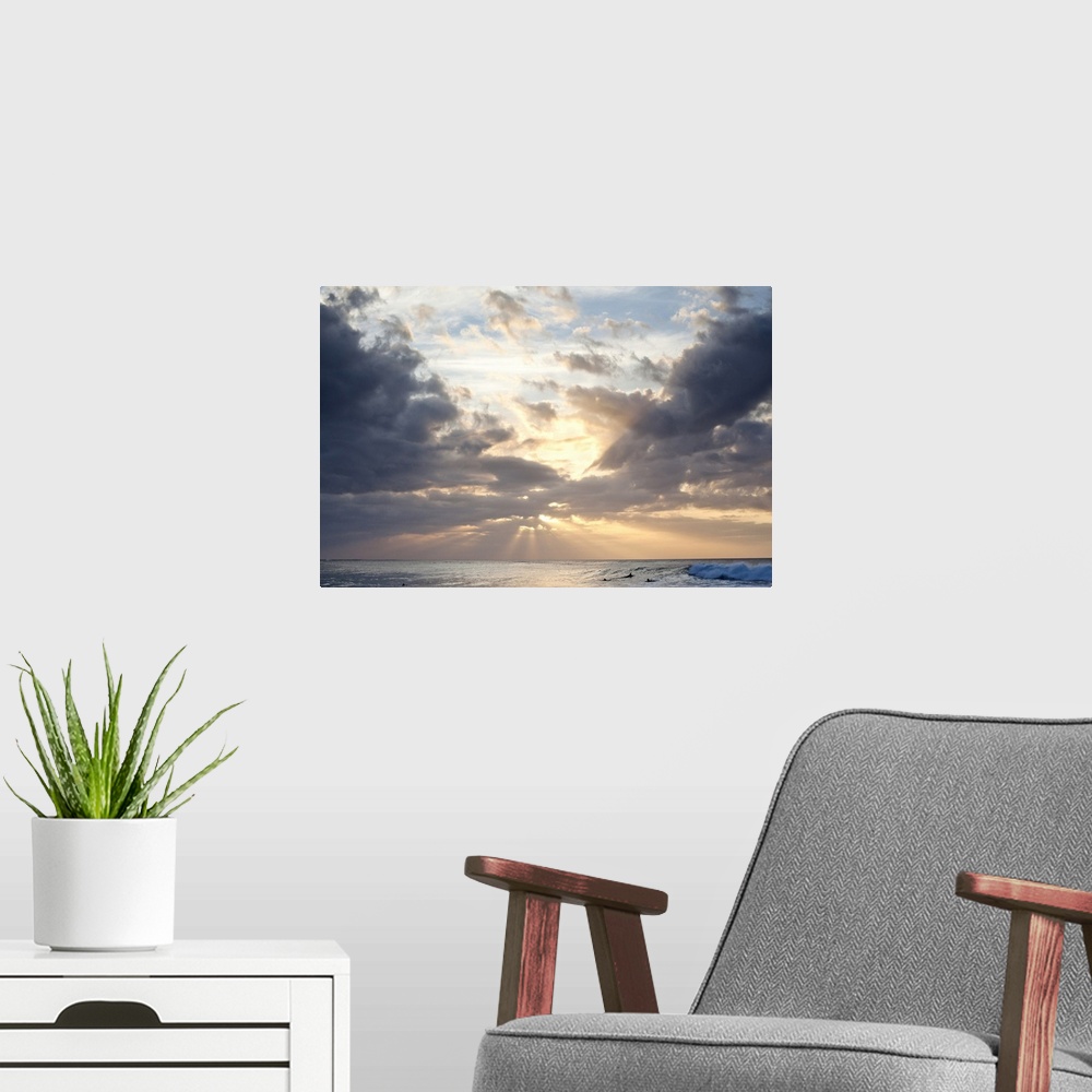 A modern room featuring Crepuscular rays of light break through the sky over the blue ocean, surfers in the background