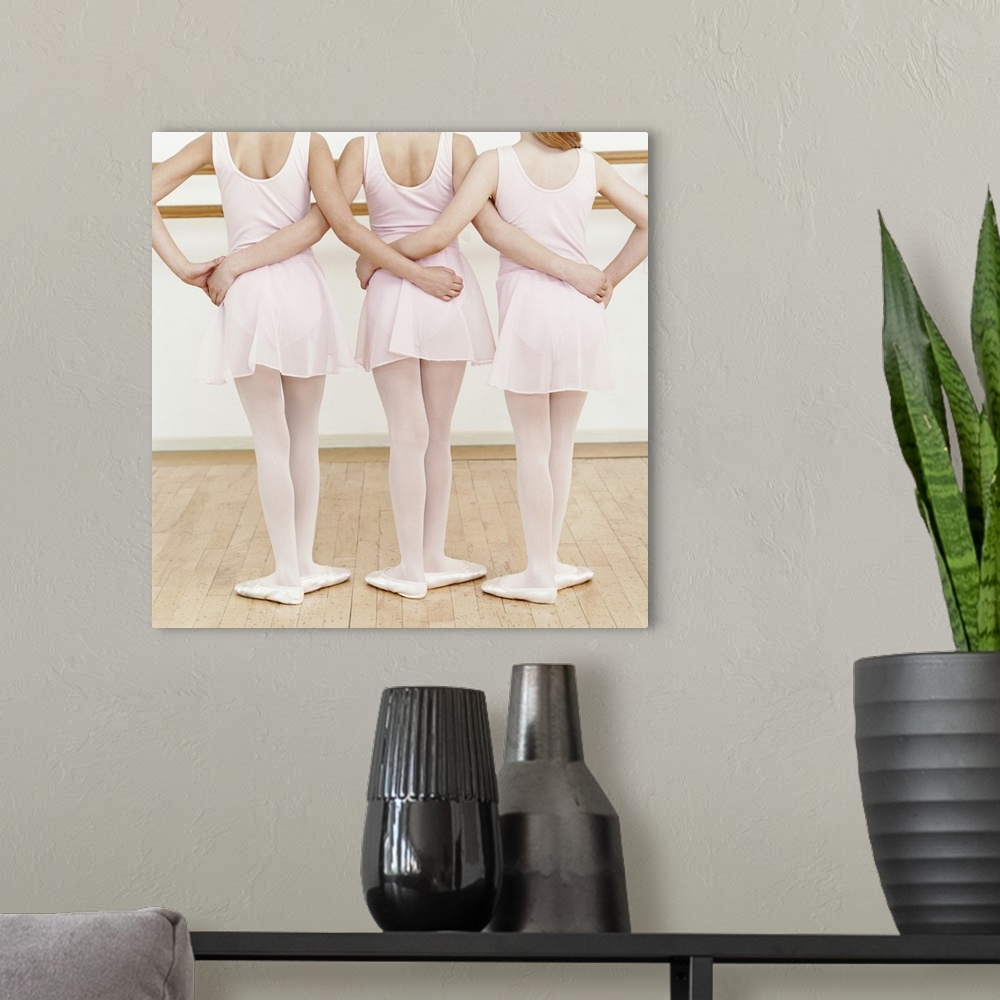 A modern room featuring Rear View of Three Young Ballet Dancers Standing in a Line With Their Arms Around Each Other