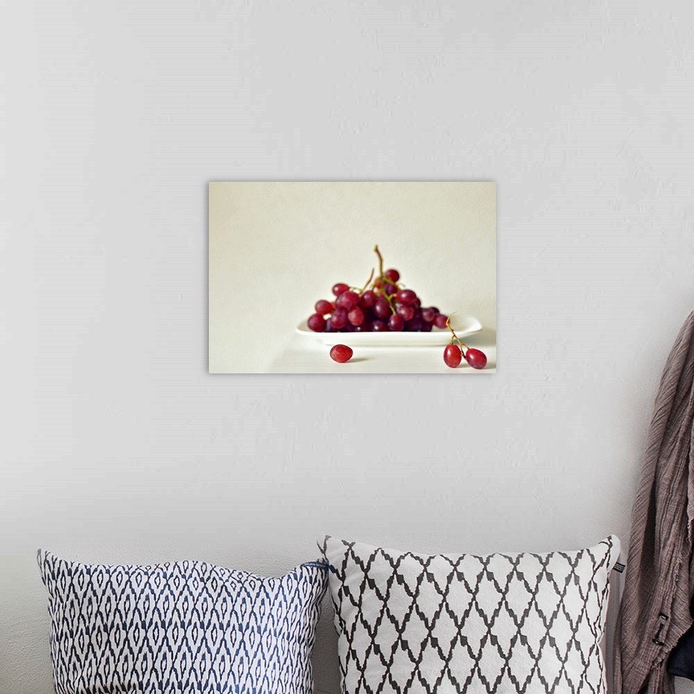 A bohemian room featuring Red grapes on white square plate on white table against white wall.