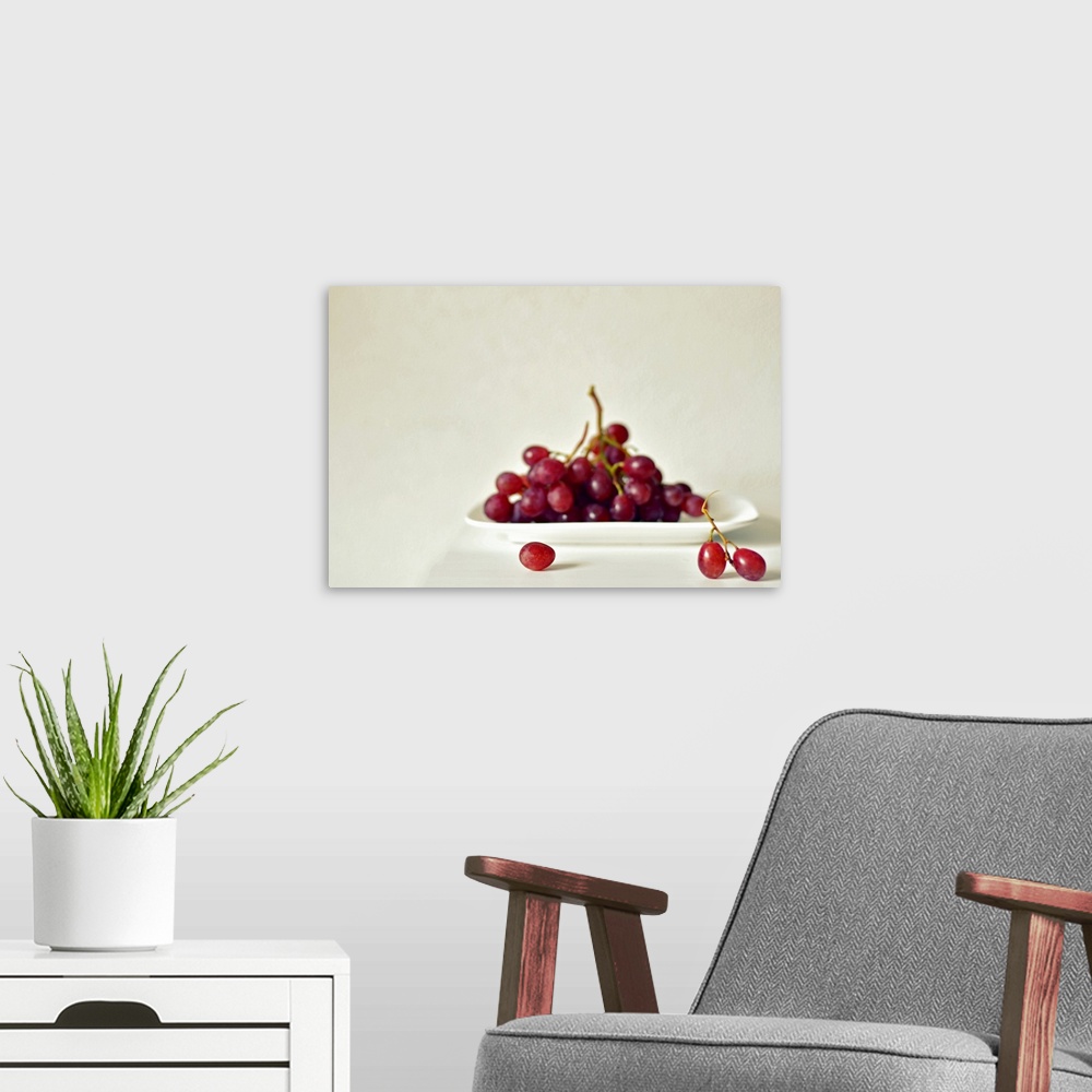 A modern room featuring Red grapes on white square plate on white table against white wall.