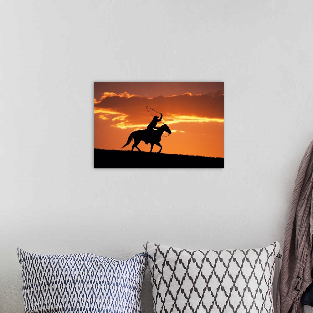 A bohemian room featuring The sunset sky silhouettes a cowboy on his horse as he swings his rope above his head.