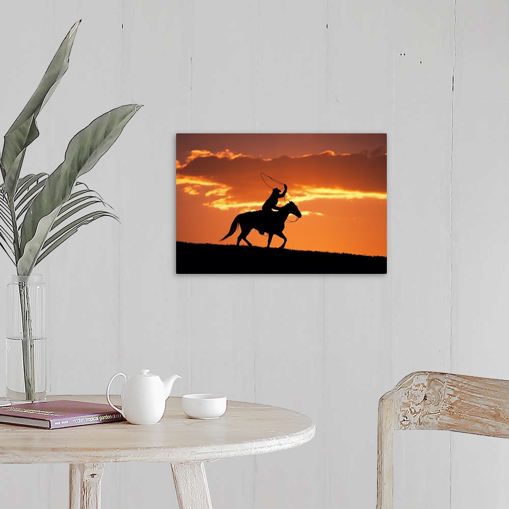 A farmhouse room featuring The sunset sky silhouettes a cowboy on his horse as he swings his rope above his head.