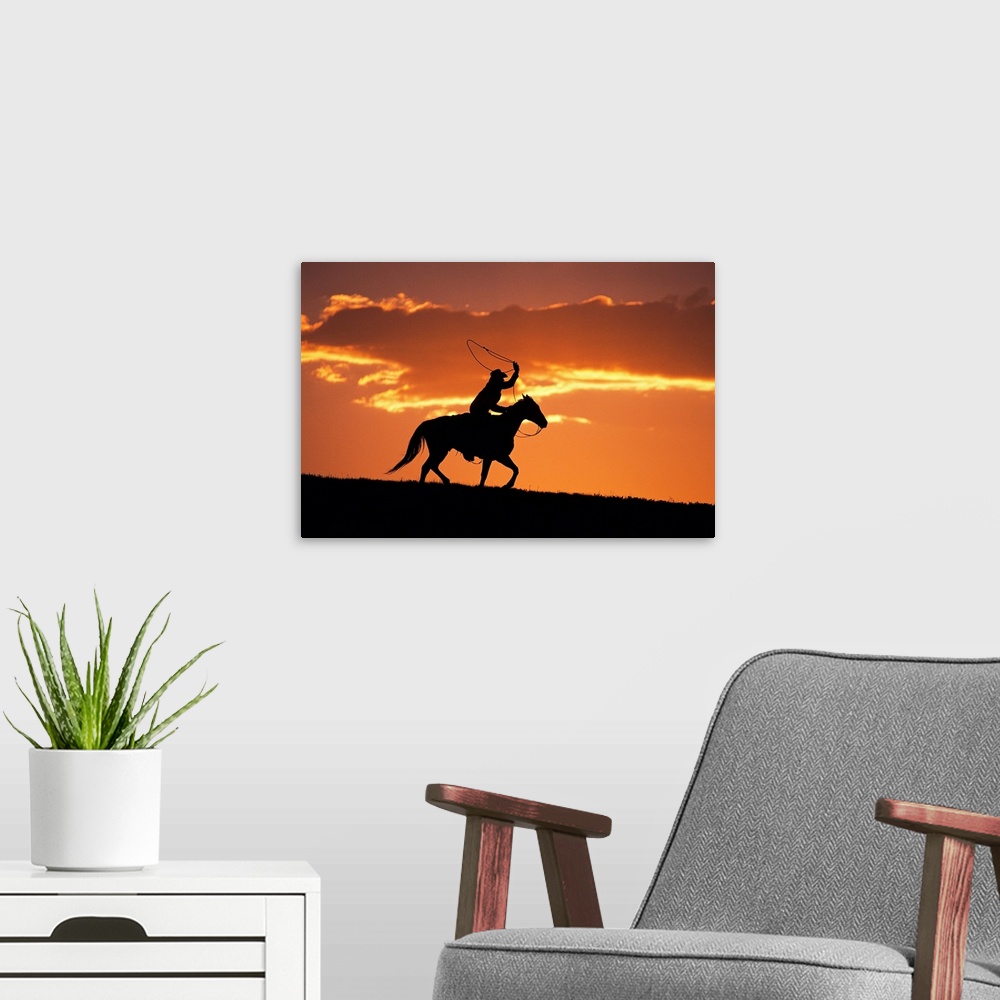 A modern room featuring The sunset sky silhouettes a cowboy on his horse as he swings his rope above his head.