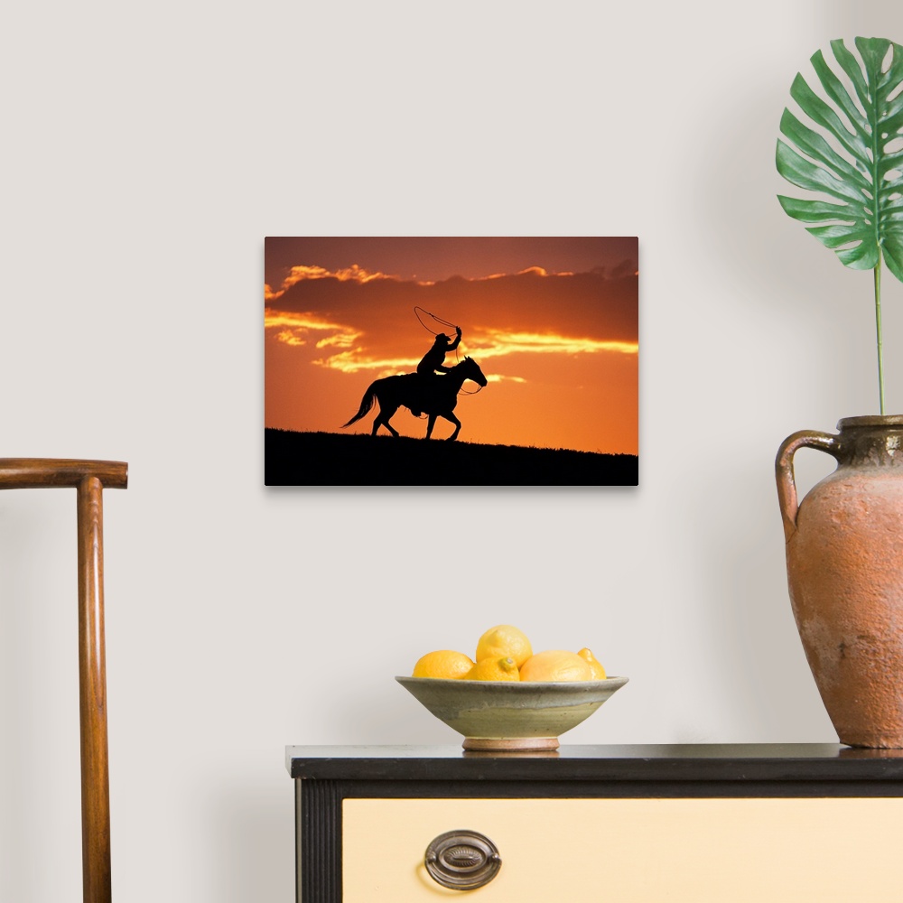 A traditional room featuring The sunset sky silhouettes a cowboy on his horse as he swings his rope above his head.