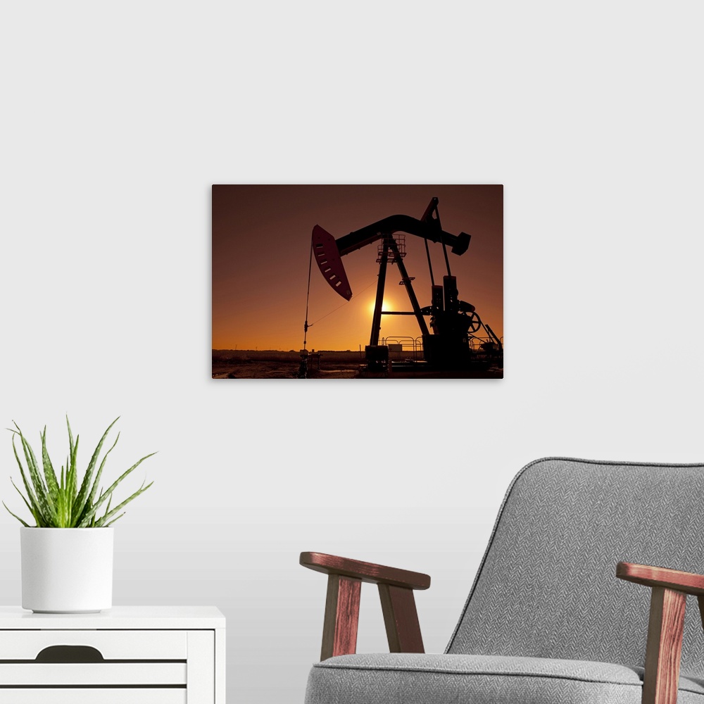 A modern room featuring Silhouette of an oil pump jack on rig as the sun sets in the background.